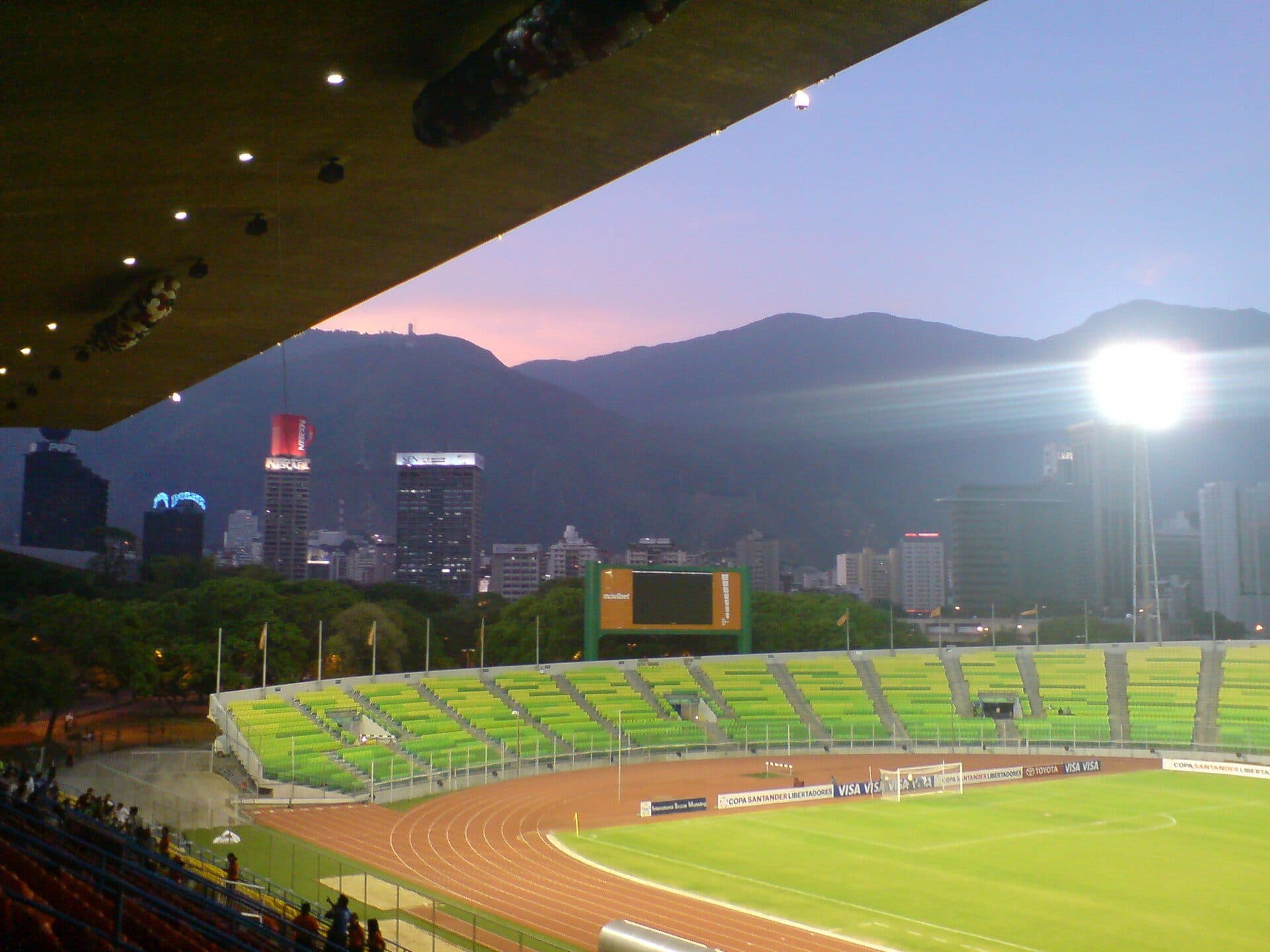 Running track, pitch and green stands of the Estadio Olímpico de la UCV at dusk, with the Ávila mountains behind