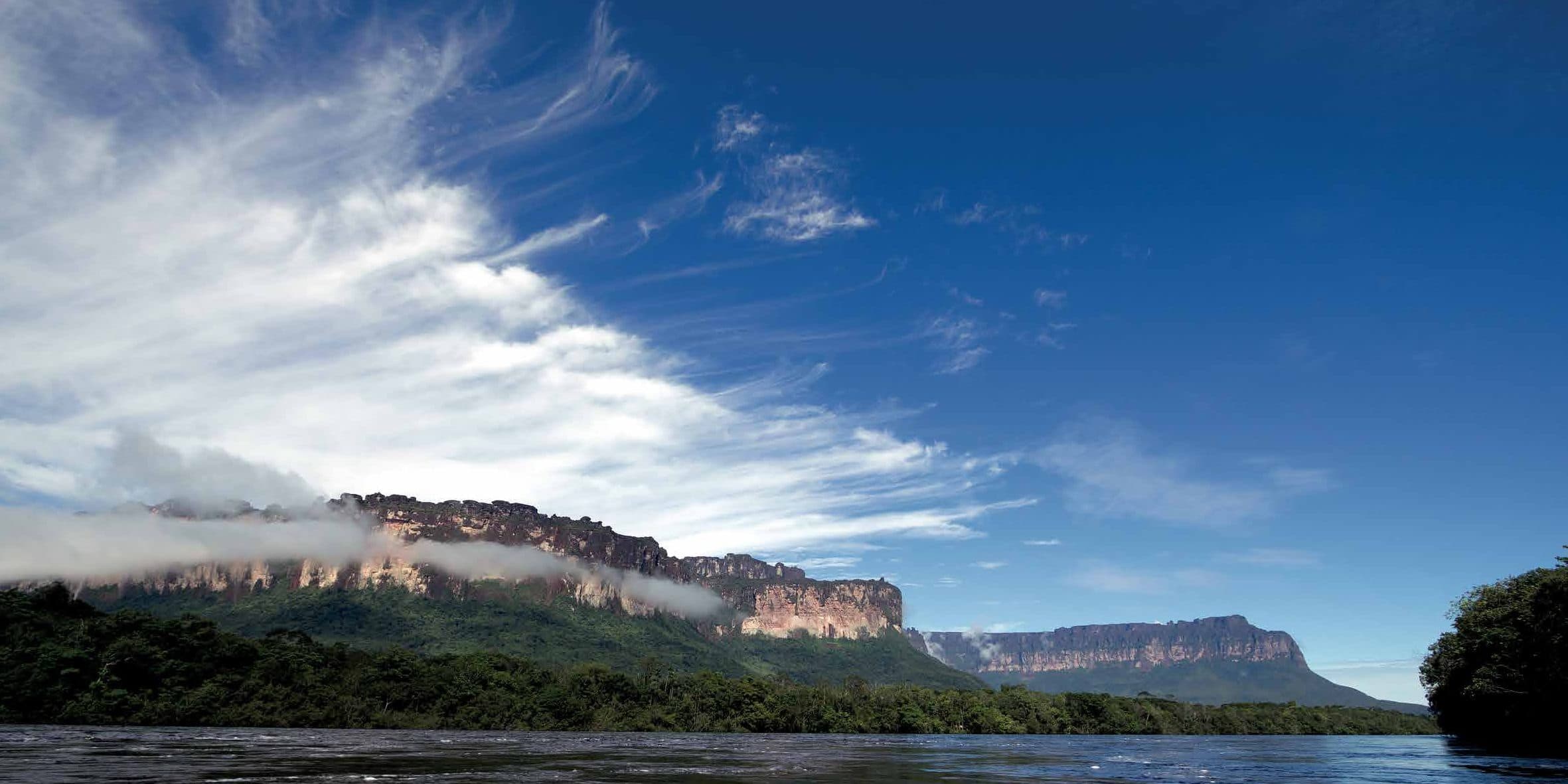 Tepui cliffs rising above a river under a deep blue sky