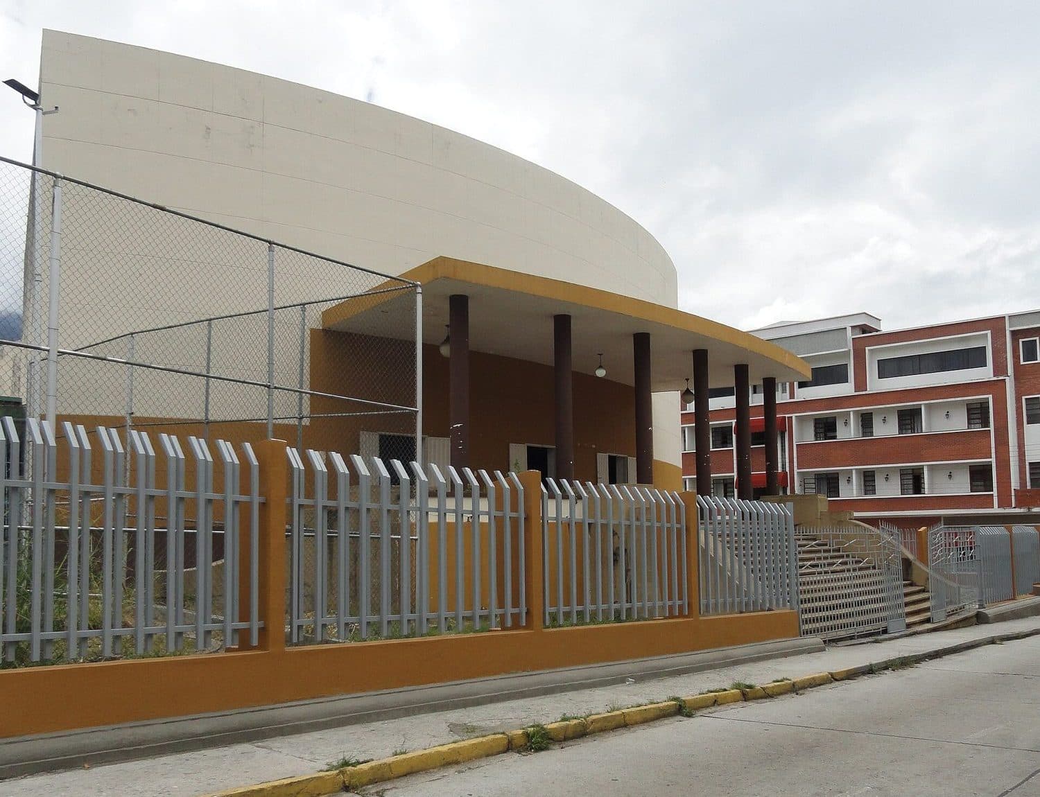 Curved auditorium volume with a columned canopy beside a brick classroom block at the Liceo Libertador in Mérida