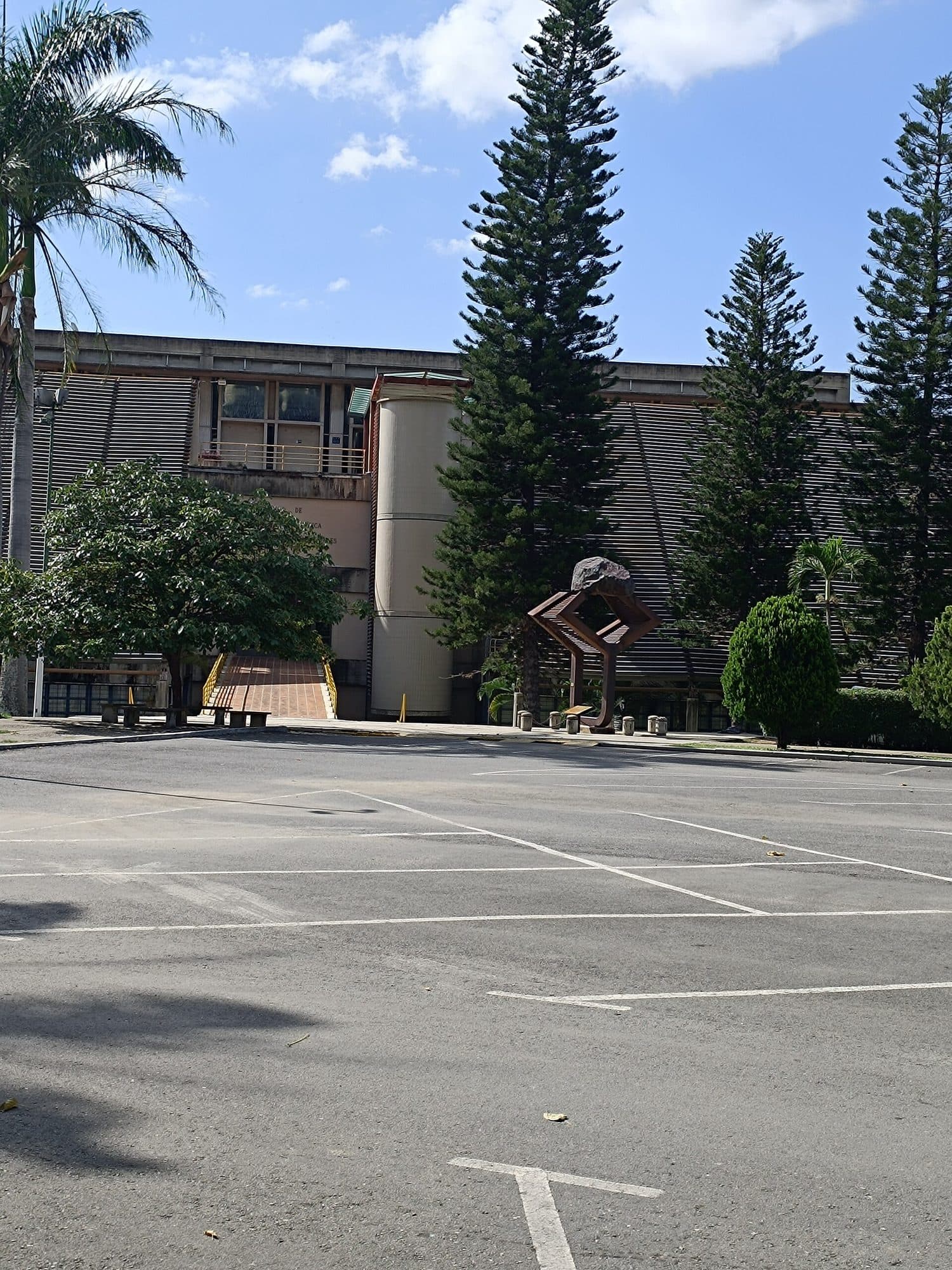 Entrance and cylindrical stair tower of the School of Metallurgical Engineering at the UCV, seen across a car park