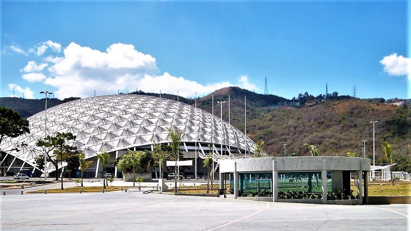 The white geodesic dome of the Poliedro de Caracas seen from its plaza, with hills behind