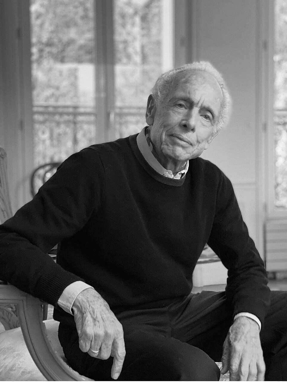 Black-and-white portrait of Jimmy Alcock, an older man in a dark sweater seated beside tall windows