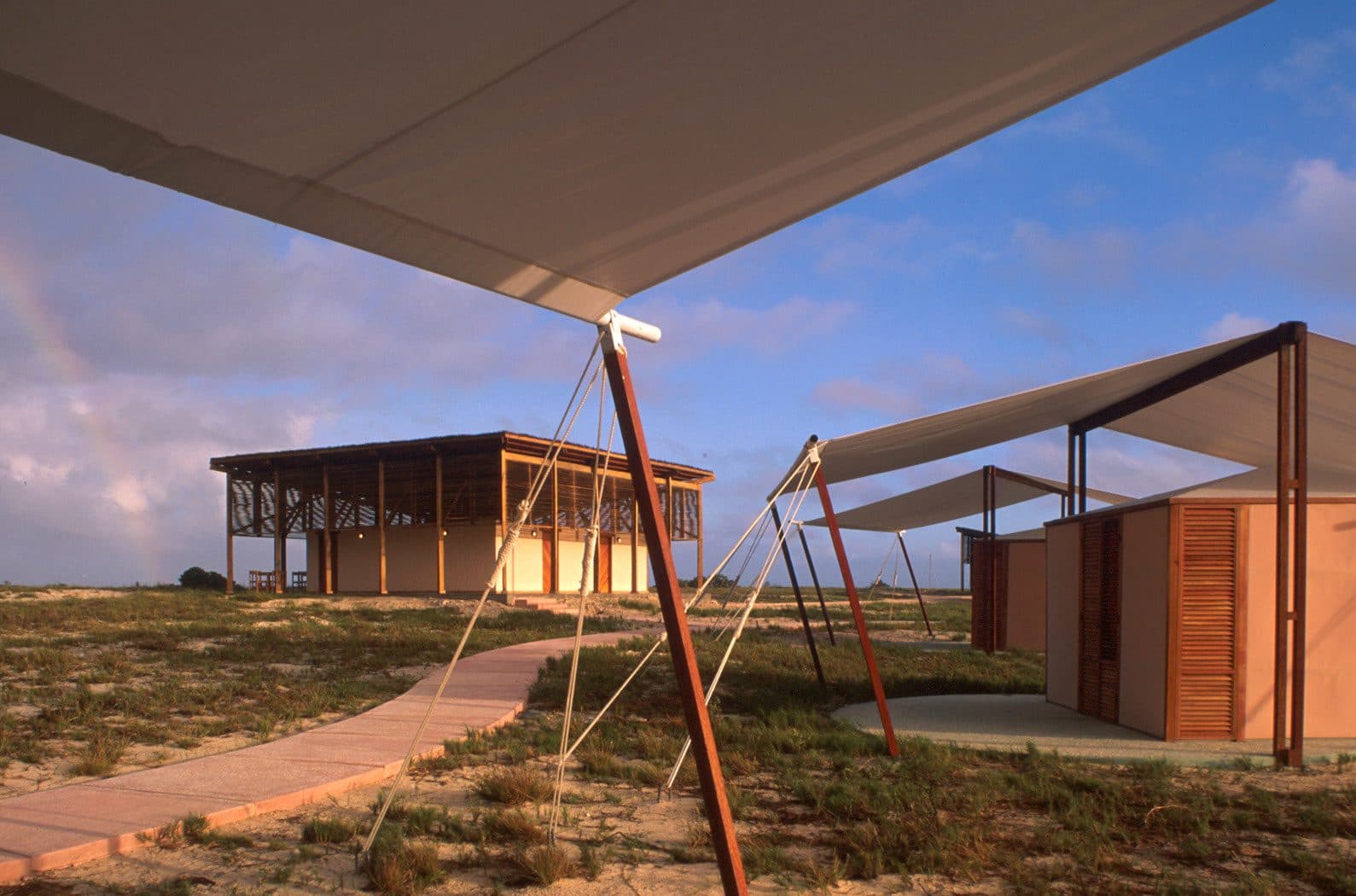 Canvas-roofed tents with wooden louvred doors and a raised timber pavilion on a sandy cay