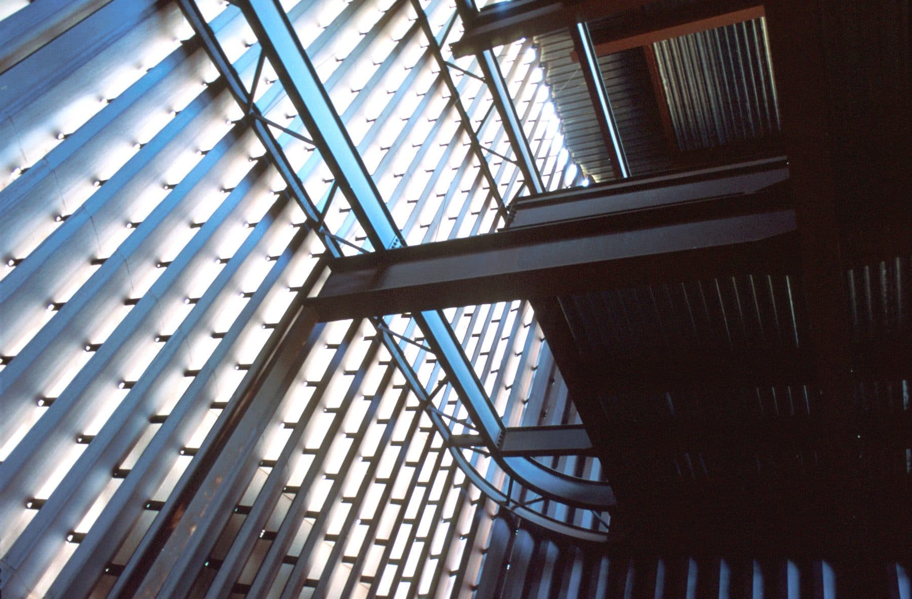 Looking up at steel beams and V-shaped steel slats that filter daylight