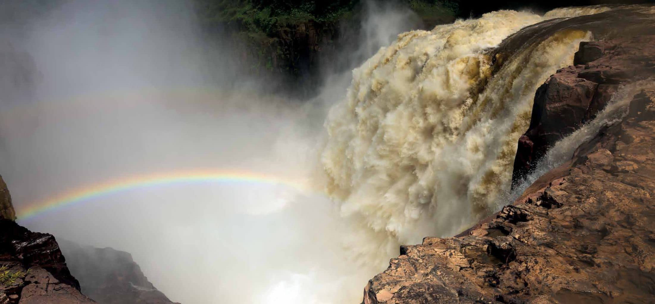 A rainbow arcing over a roaring, sediment-brown waterfall
